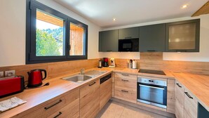Eine moderne Küche mit Holzschränken, einem eingebauten Backofen, einer Mikrowelle und einem Fenster mit Blick auf Grünflächen.
