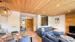 Ein modernes Wohnzimmer mit einer Sofagarnitur, einem Esstisch mit Stühlen und einem Fernseher.