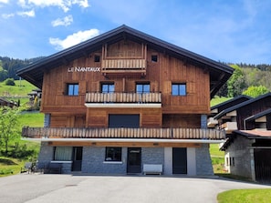 A wooden chalet with a balcony, stone foundation, and a sign reading 'LE NANTAUX'.