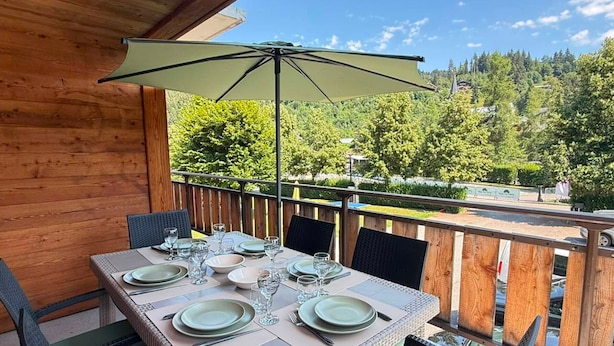 Eine Holzterrasse mit Esstisch, mit Blick auf ein bewaldetes Gebiet.
