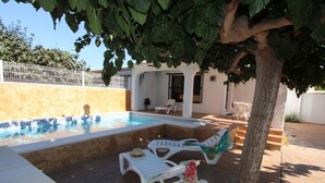 A pool area with white lounge chairs, a tiled pool, and a stone wall. - Cozy Beach Home: Free WiFi, Optional AC, Pet-Friendly, Dog Beach Nearby (Deltebre)