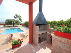 A brick outdoor kitchen with a chimney, a swimming pool, and a patio area with chairs and potted plants.
