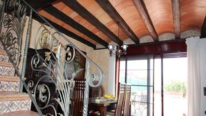 Een trap met versierde metalen leuningen, een eethoek met een tafel en stoelen, en een groot raam met uitzicht op de omgeving.