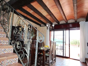 A staircase with ornate metal railings, a dining area with a table and chairs, and a large window with a view of the outdoors.