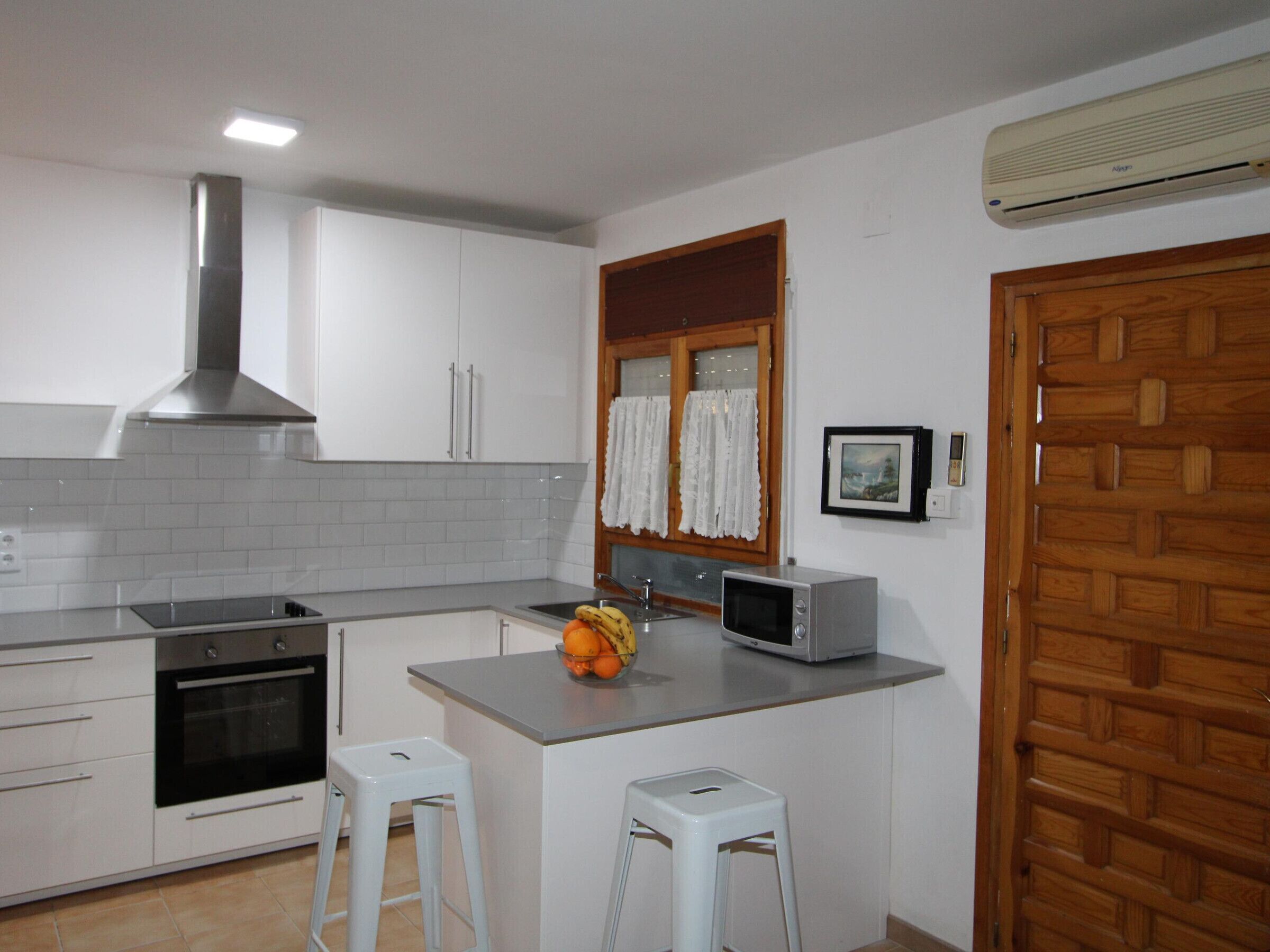 A kitchen with white cabinets, a stainless steel range hood, a microwave, and a small island with stools.