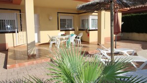 Un patio con mesa y sillas, techo de paja y una planta de palmera.