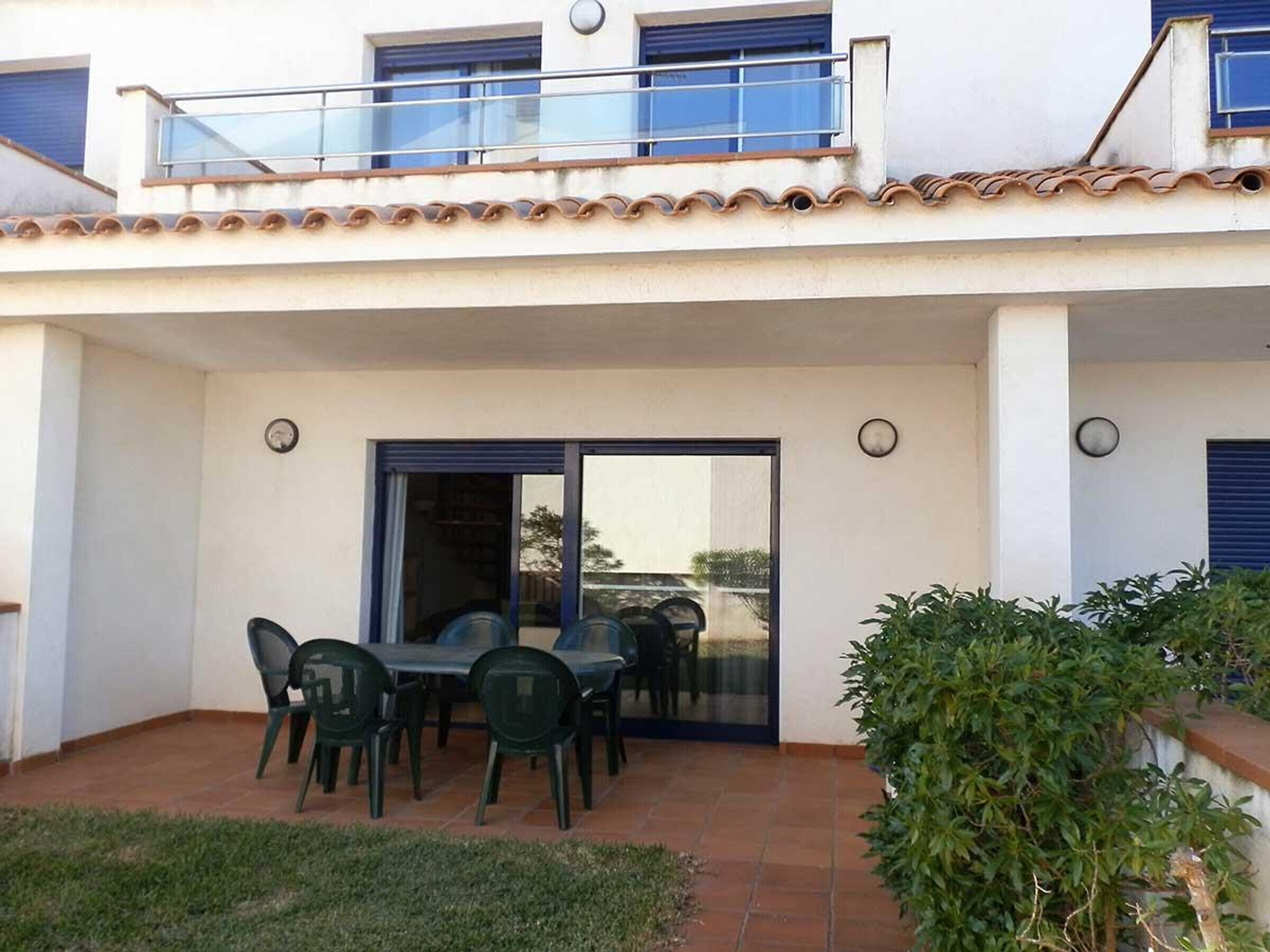 Une terrasse couverte avec une table et des chaises, une porte vitrée et un petit espace jardin.