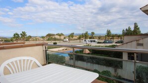Un balcón con mesa y sillas, con vista a un estacionamiento con vehículos y una piscina.