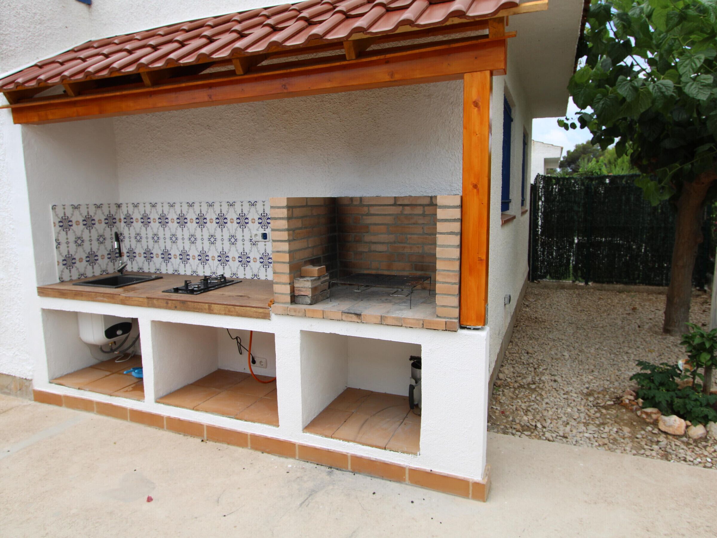 An outdoor kitchen with a tiled backsplash, a brick oven, and a wooden pergola.