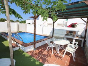 A swimming pool with a wooden deck, a barbecue area, and a small table with chairs.