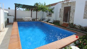 Piscina com borda azulejada, área de estar coberta e parede de pedra.