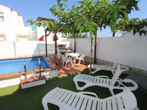 A pool with a diving board, white lounge chairs, and a small table with chairs.
