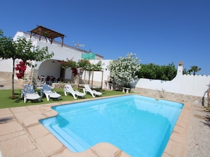 Una piscina con sillones de descanso, una pérgola y un muro de piedra.