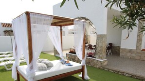 A four-poster bed with white linens and a canopy, set on artificial grass, with a stone wall and outdoor furniture in the background. - Family-Friendly Home with Pool, Near Beach, Pet Friendly, Free WiFi, Opt. AC (Deltebre)