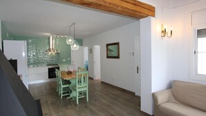 A spacious living area with a wooden ceiling, a dining table with chairs, a sofa, and a kitchen with green tiles and pendant lights. - Beachside Family Home: Private Pool, Free Wi-Fi, Pets Welcome, Near Dog-Friendly Beach (Deltebre)
