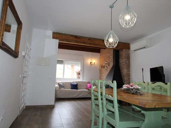 Un coin repas avec une table et des chaises en bois, un mur en briques et une fenêtre avec des stores.
