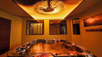A spa room with a hot tub, wooden flooring, and a ceiling light fixture.
