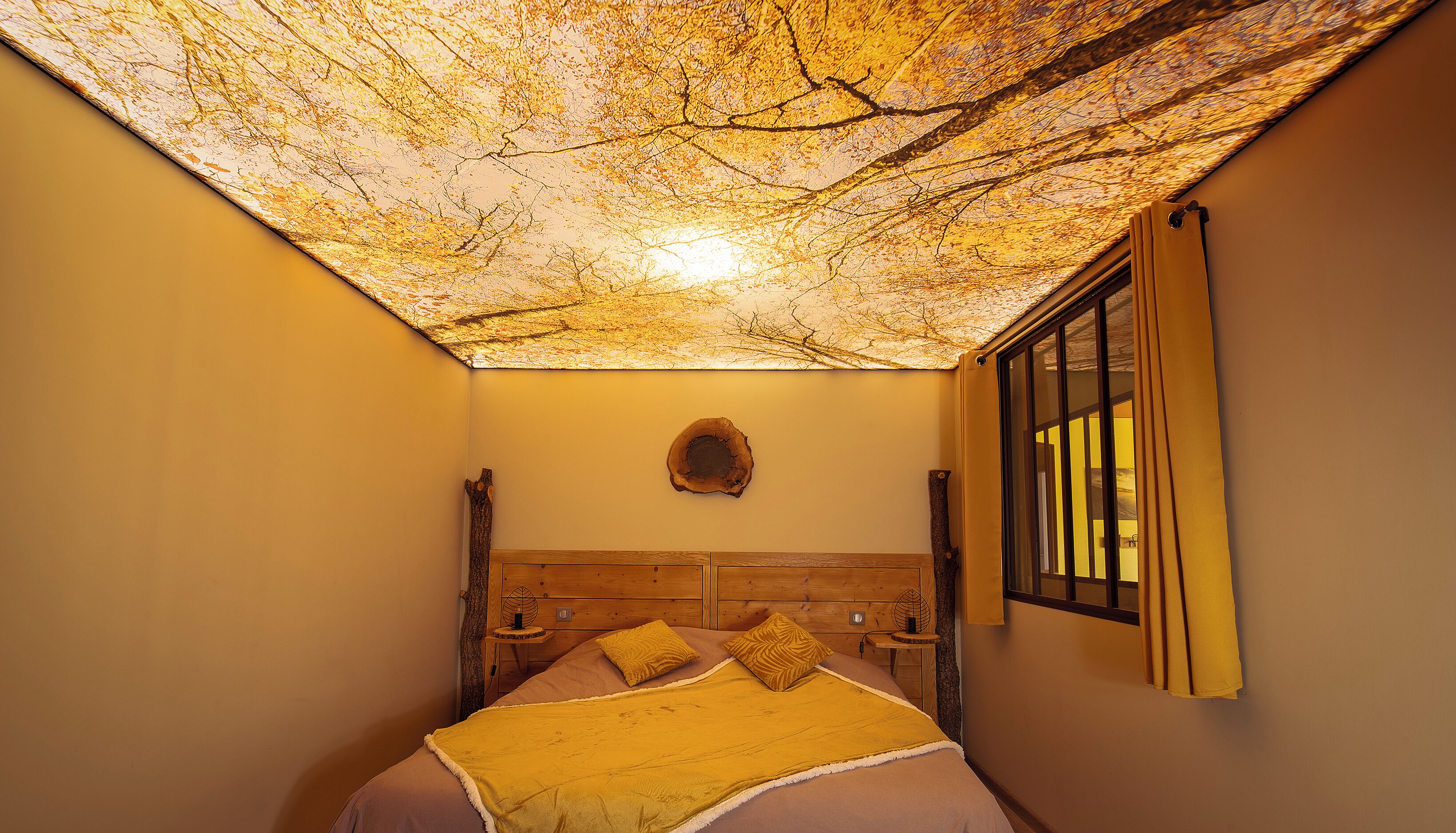 A room with a bed, a wooden headboard, a wall-mounted circular object, and a window with curtains.