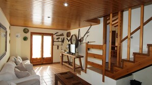 Un salon avec un plafond en bois, un canapé, une table basse, un téléviseur posé sur un meuble en bois et un escalier.