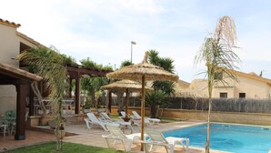 Une piscine avec des chaises longues, une pergola dotée d’un toit de chaume et une pelouse bien entretenue.