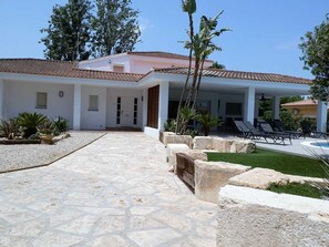 A modern house with a tiled roof, a stone pathway leading to the entrance, and a pool area with lounge chairs. - Cozy Beachside House: Private Pool, Free WiFi, Pet-Friendly, Near Dog Beach (Deltebre)