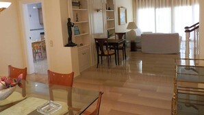 Een ruime woonkamer met een eettafel, stoelen, een bank en een boekenkast.