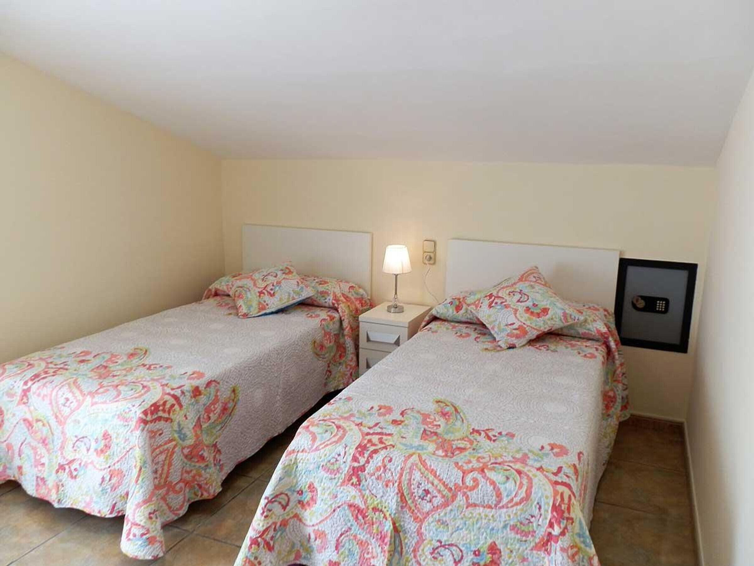 Ein Hotelzimmer mit zwei Einzelbetten, jeweils mit einem floralen Bettbezug, einem Nachttisch mit Lampe sowie einem fest montierten Safe.
