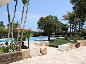 A pool area with stone flooring, palm trees, and a well-maintained lawn. - Cozy Beachside House: Private Pool, Free WiFi, Pet-Friendly, Near Dog Beach (Deltebre)