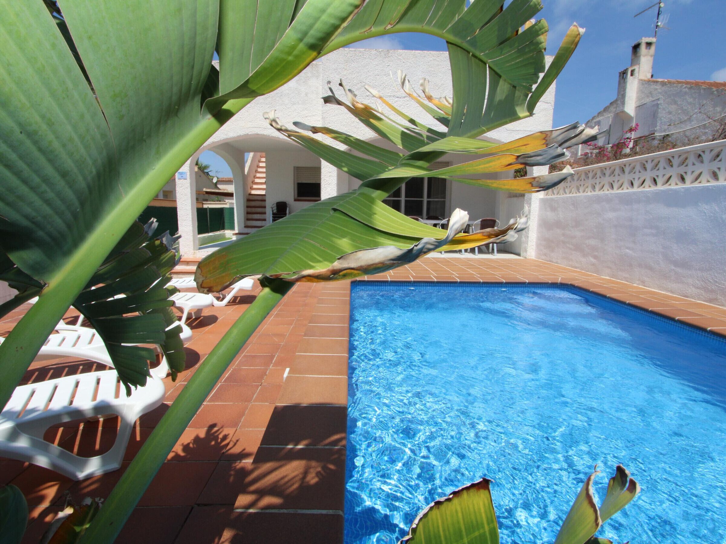 A swimming pool with clear blue water, surrounded by a tiled patio area.