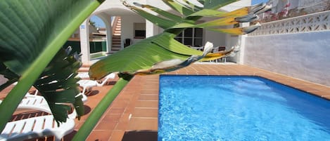 A swimming pool with clear blue water, surrounded by a tiled patio area.