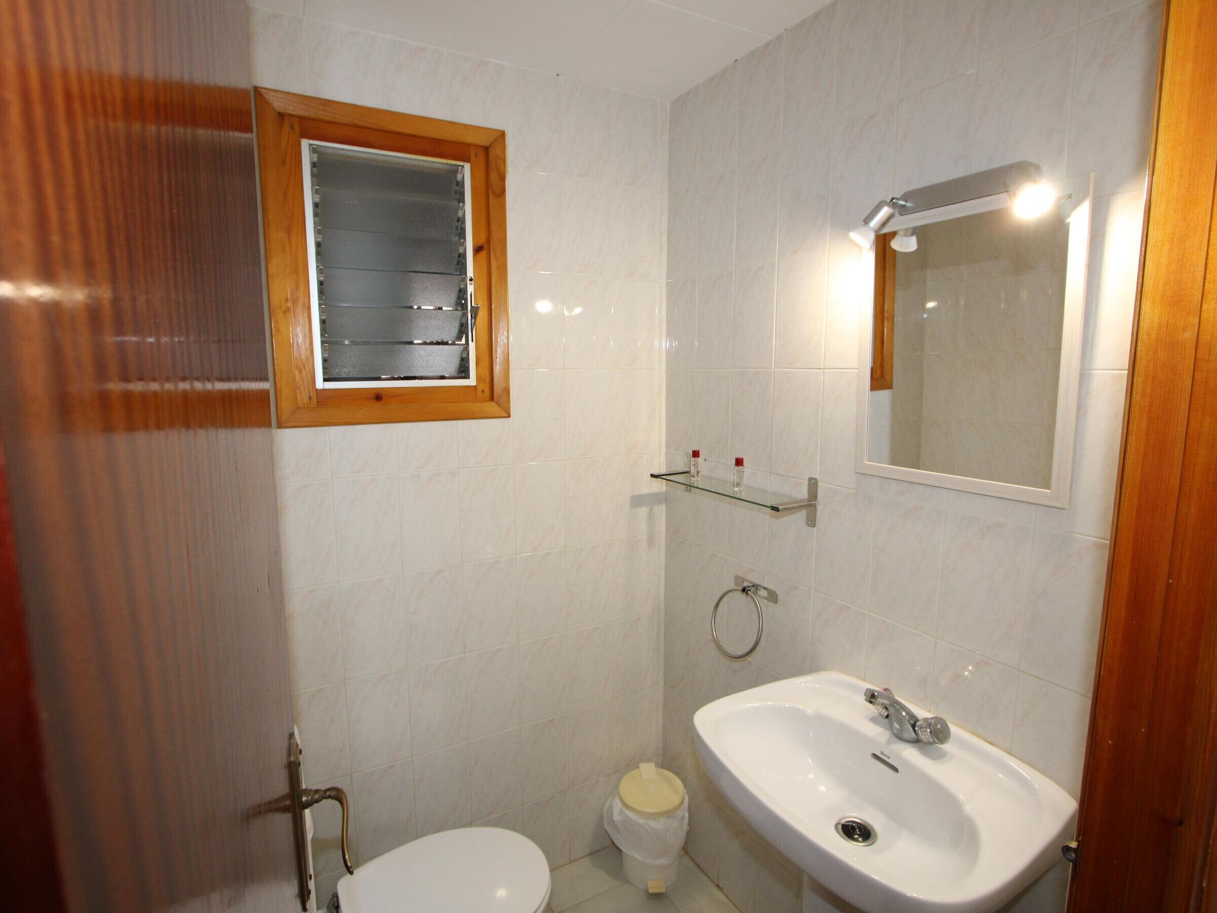 A small bathroom with a toilet, a sink, a mirror, and a window.