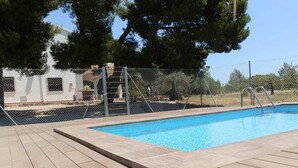 Une piscine dotée d’une terrasse en bois, entourée d’une clôture en treillis métallique et d’arbres.
