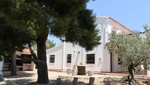 Un bâtiment blanc avec un toit en tuiles, entouré d’arbres et bordé d’une cour en gravier.