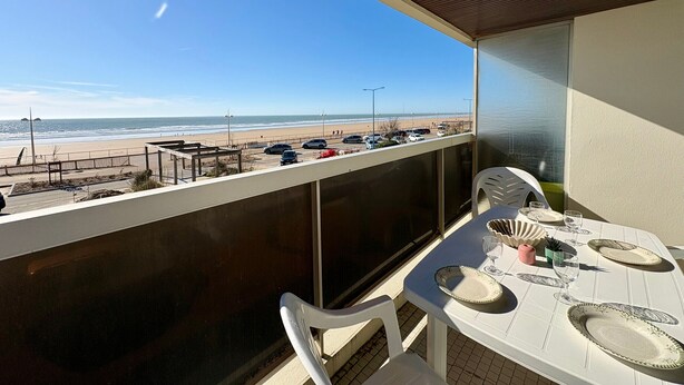 Ein Balkon mit Esstisch, Blick auf einen Strand mit Autos und einem Zaun.