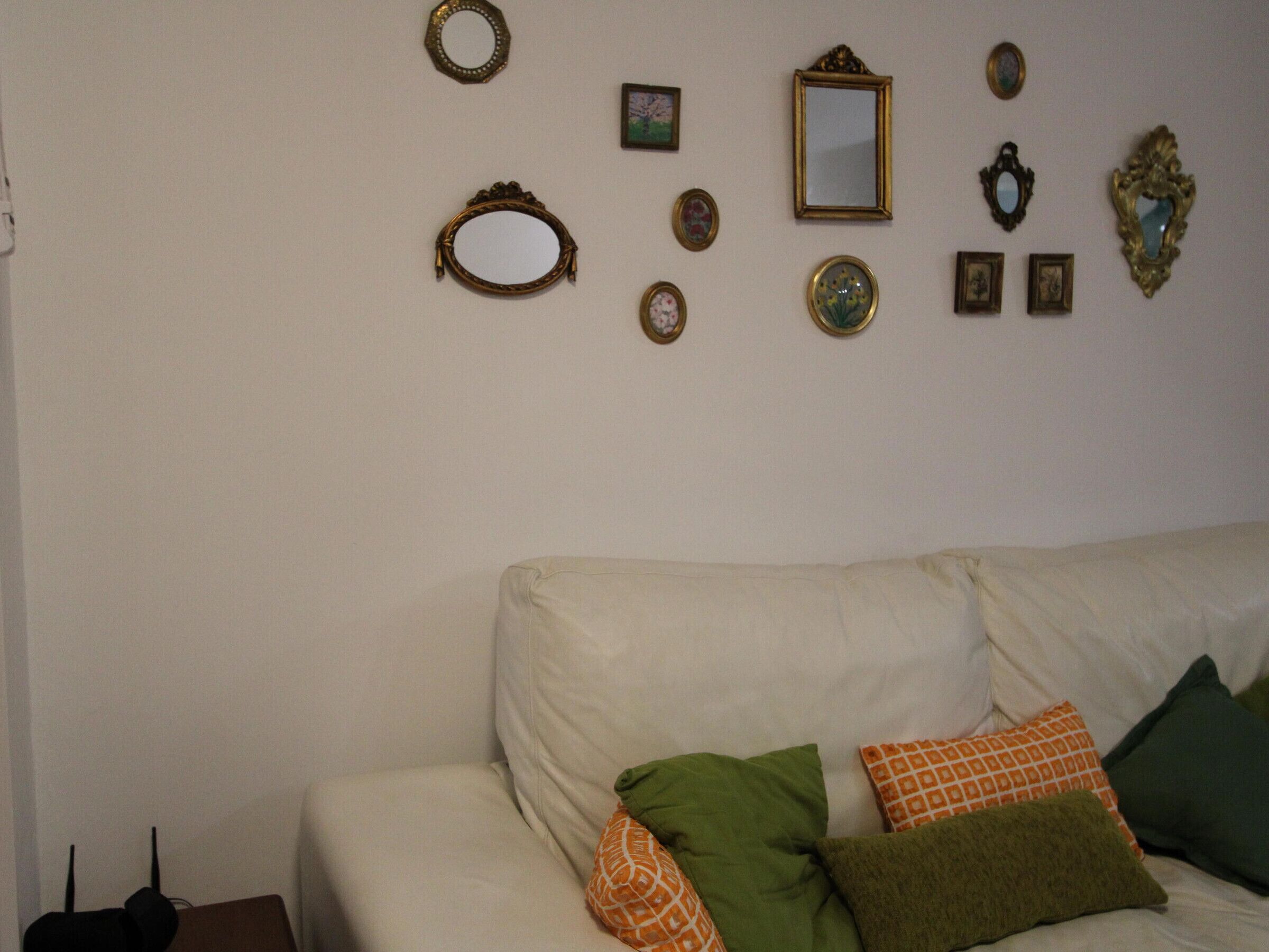 A living room with a white sofa, several decorative mirrors, and a few framed pictures on the wall.
