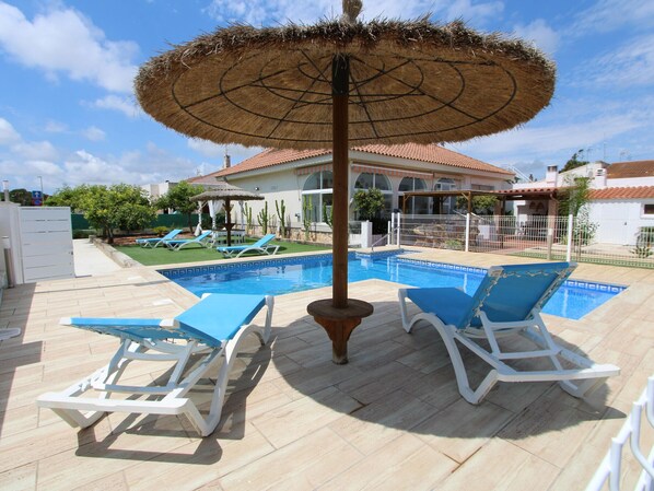 A swimming pool with blue tiles, two white lounge chairs, and a thatched umbrella. - Family Haven Near the Sea: Private Pool, Pet-Friendly, Wi-Fi, Optional A/C (Deltebre)