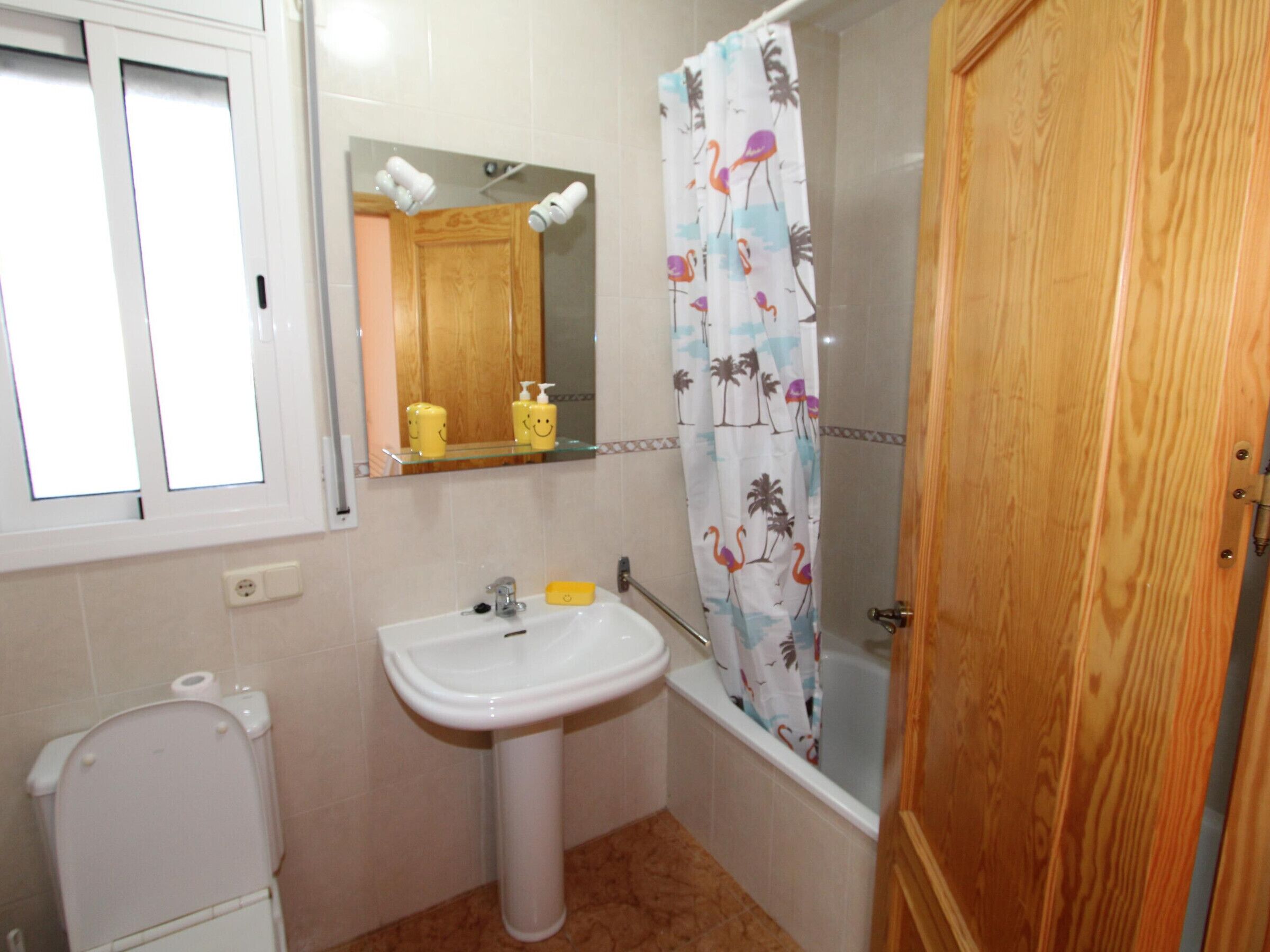 Une salle de bain avec un lavabo blanc, des toilettes, un miroir et un rideau de douche à motifs tropicaux.