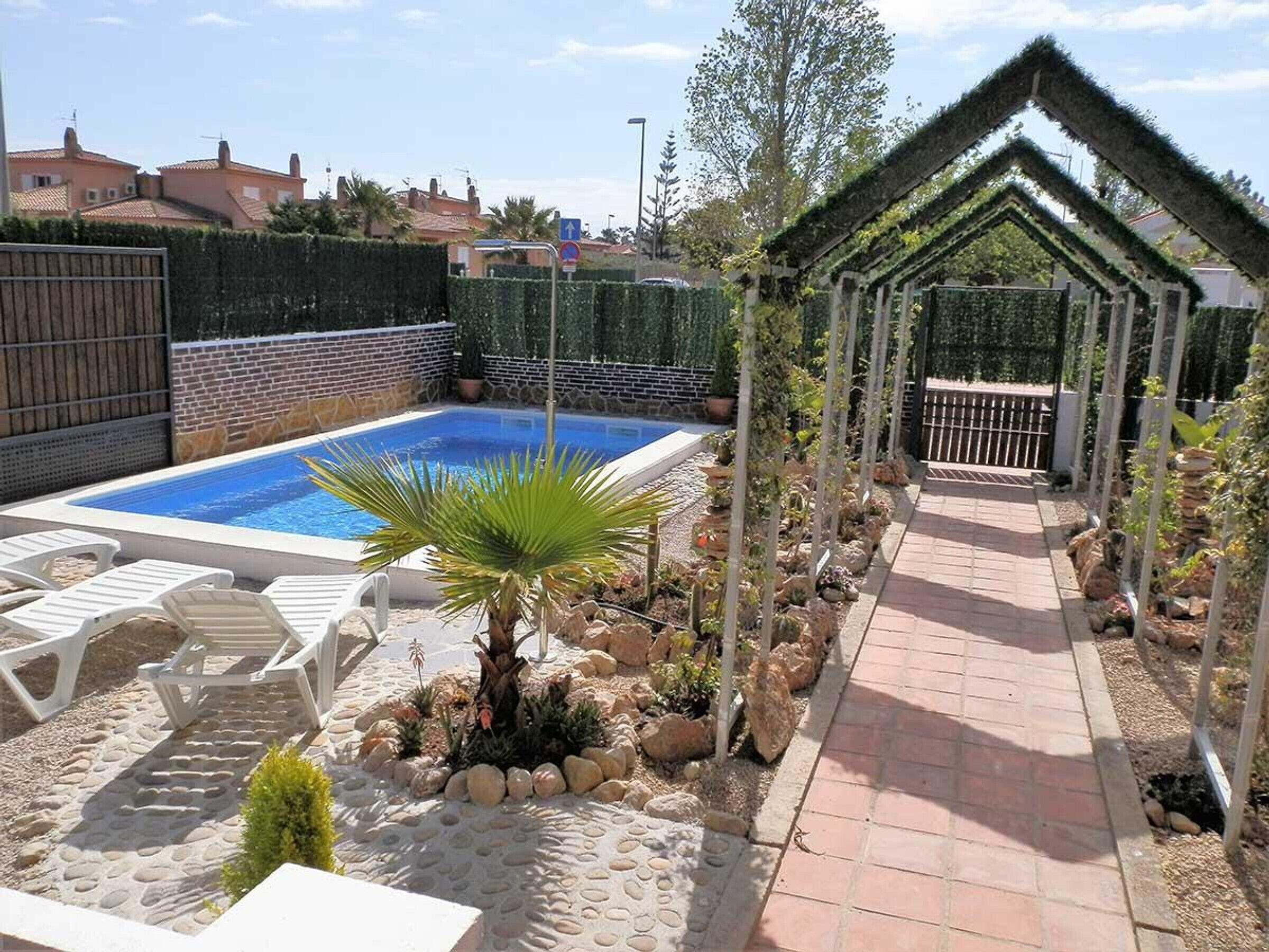 Ein Schwimmbecken mit Liegestühlen, ein Garten mit Steinen und Pflanzen sowie eine Pergola.