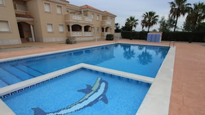 Una piscina con un mosaico de delfín, rodeada por un edificio con balcones y palmeras.