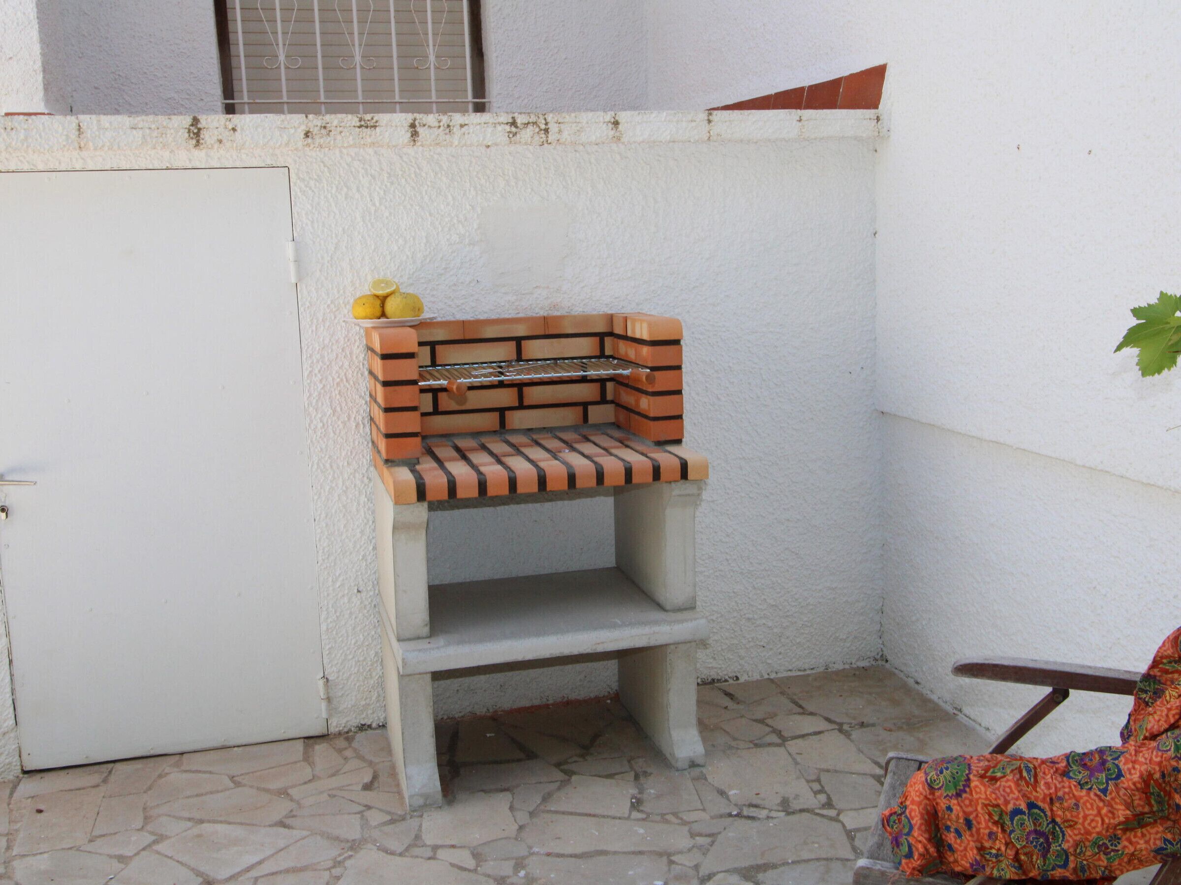 A small outdoor area with a brick barbecue grill, a white door, and a tiled floor.