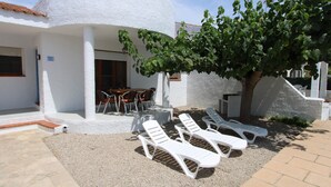Un edificio blanco con un porche cubierto, asientos al aire libre y un árbol.