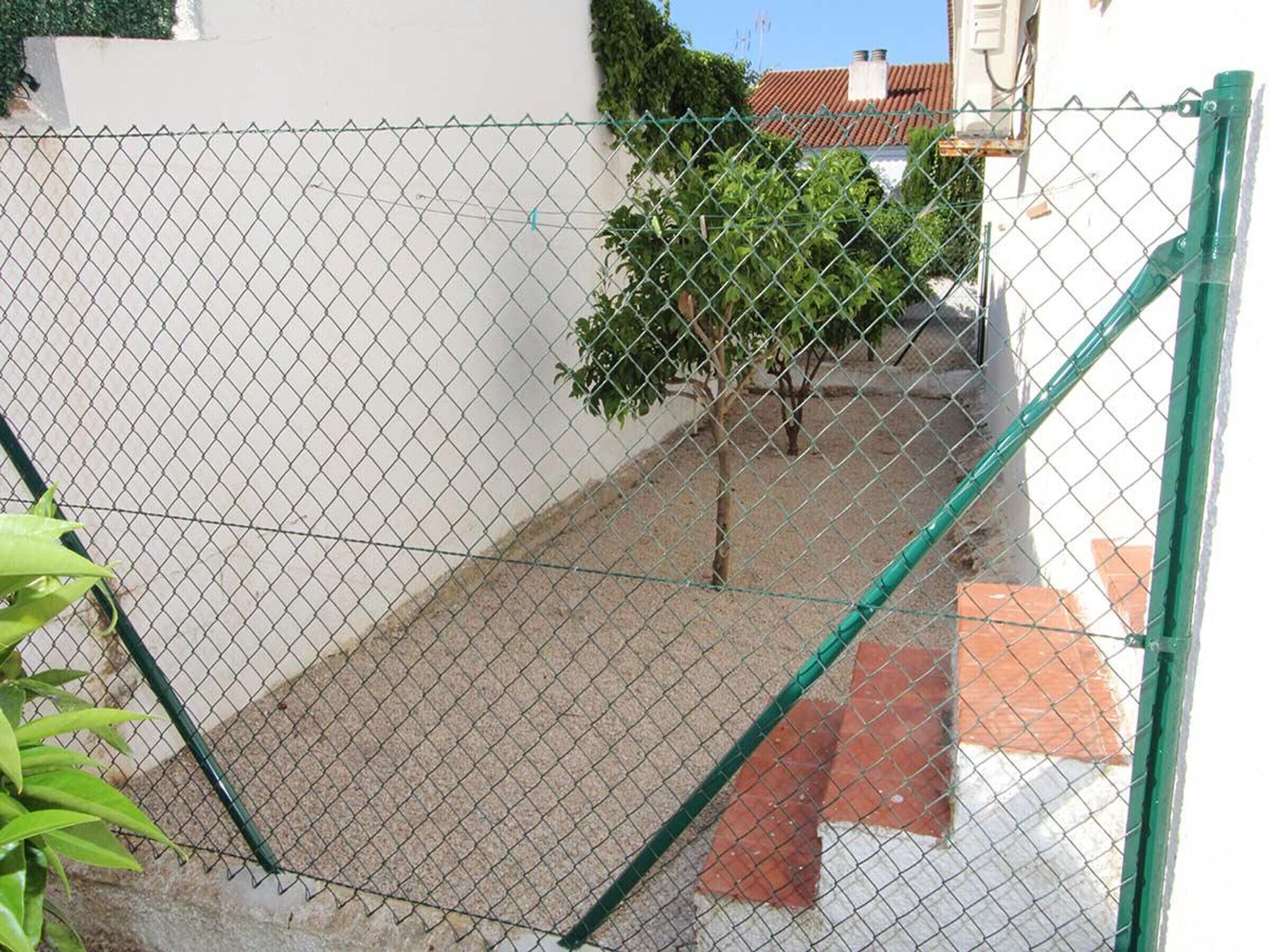 A chain-link fence with a small tree and a building in the background.