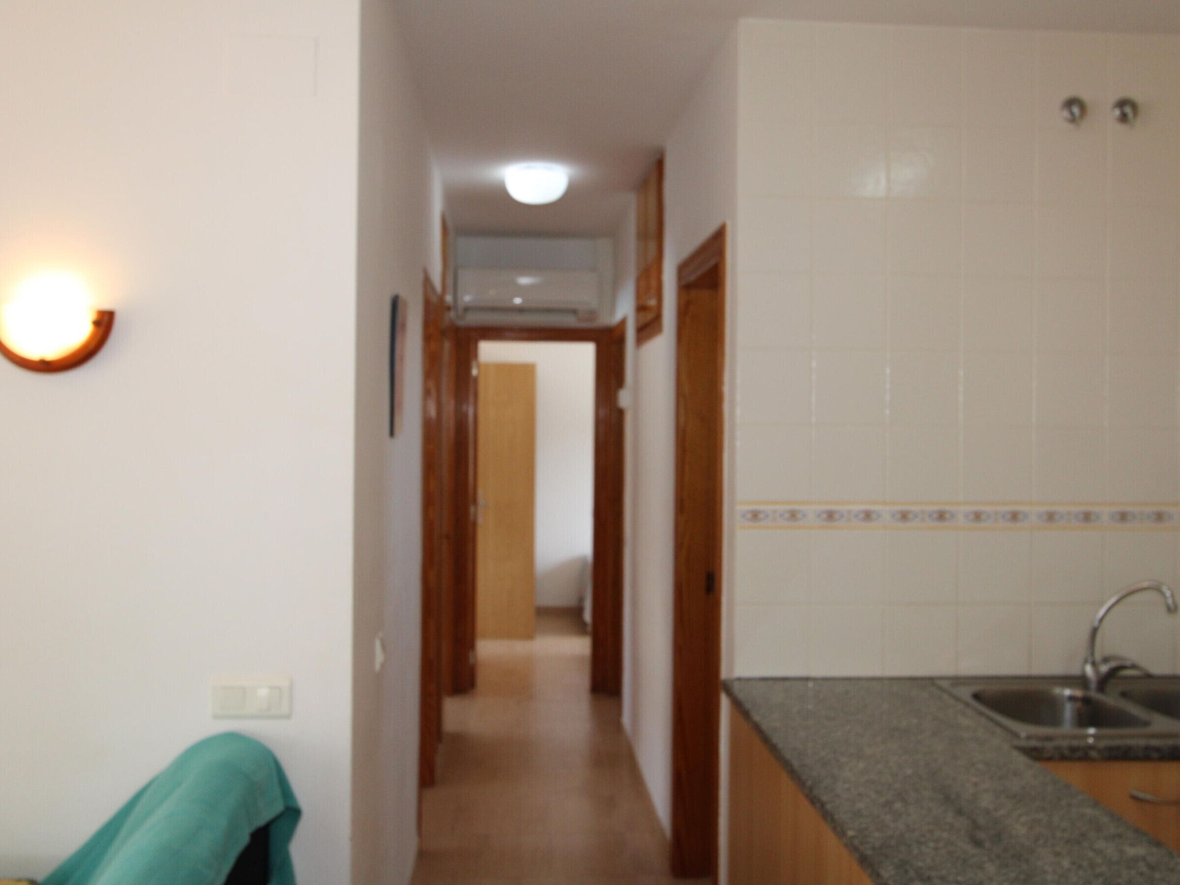A narrow hallway leading to a kitchen with a sink and cabinets.