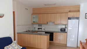 Kompakti keittiö, jossa on puukalusteet, sisäänrakennettu mikroaaltouuni ja jääkaappi.