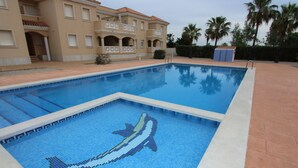 En swimmingpool med en mosaik som föreställer en delfin, omgiven av en byggnad med balkonger och palmer.