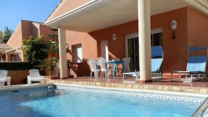 Piscina con sillas de descanso blancas y un patio techado.