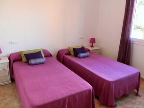 A room with two beds, each with a purple bedspread and pillows, a small bedside table with a lamp, and a window with curtains. - Beachside Oasis: Private Pool, Pet Friendly, Free WiFi, Optional A/C, Dog Beach Nearby! (Deltebre)