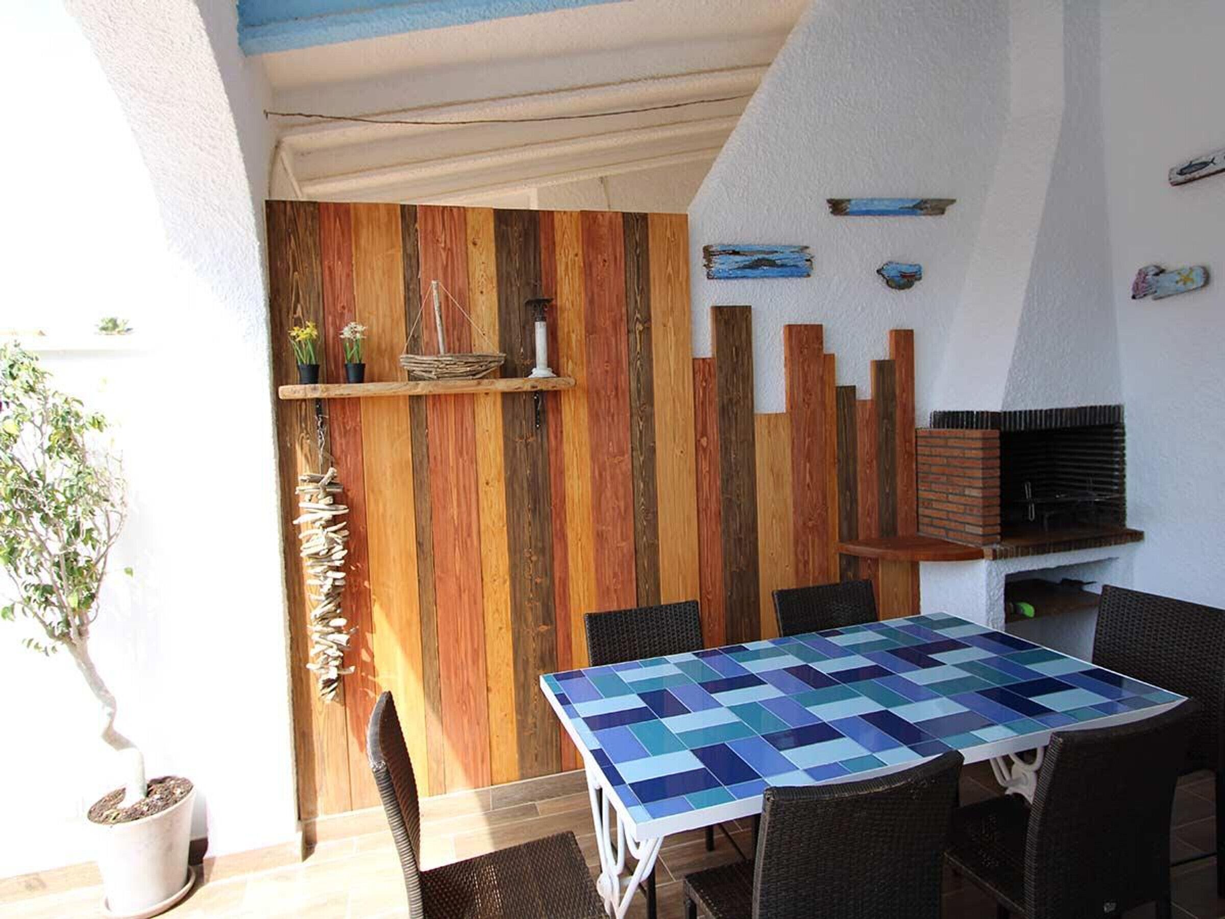 A patio area with a wooden wall, a table with a blue and white checkered tablecloth, and wicker chairs.