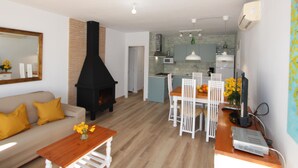 A modern living room with a fireplace, a dining area with white chairs, and a kitchen in the background. - Beachside Getaway: Private Pool, Free WiFi, Pet Friendly, Air Con, Near Dog Beach (Deltebre)