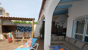 A patio with a barbecue, a lounge chair, a table with a bowl of oranges, and a sofa. - Beachside Getaway: Private Pool, Free WiFi, Pet Friendly, Air Con, Near Dog Beach (Deltebre)